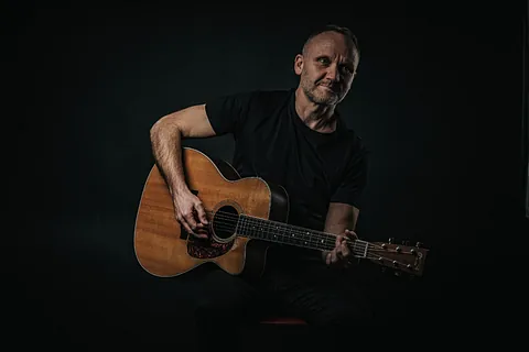 Mann med svart t-skjorte og brun akustisk gitar
