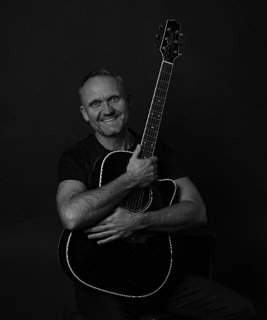 Sort-hvitt bilde av mann med svart akustisk gitar