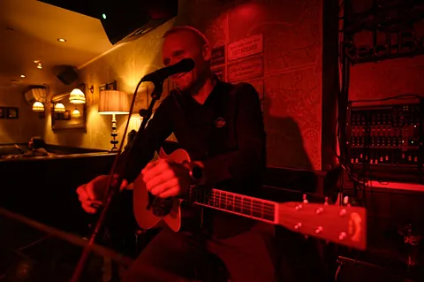 Mann med gitar foran mikrofon i rød belysning