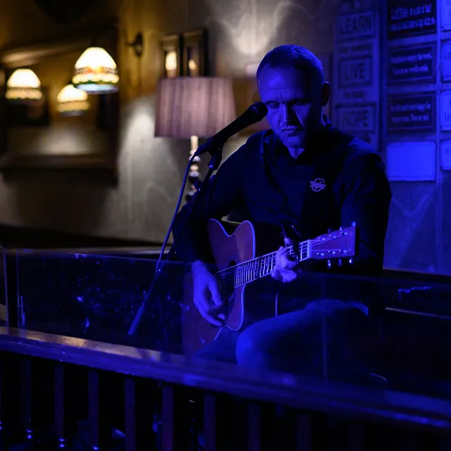 Mann med gitar foran mikrofon i blå belysning